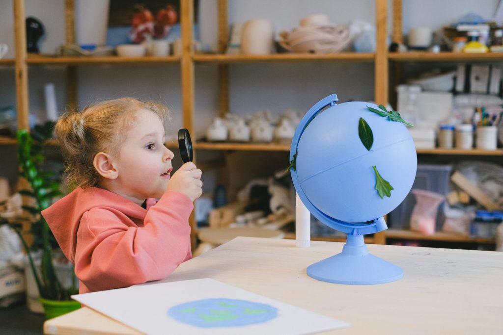 A curious child examines a globe with a magnifying glass, symbolizing learning and exploration.